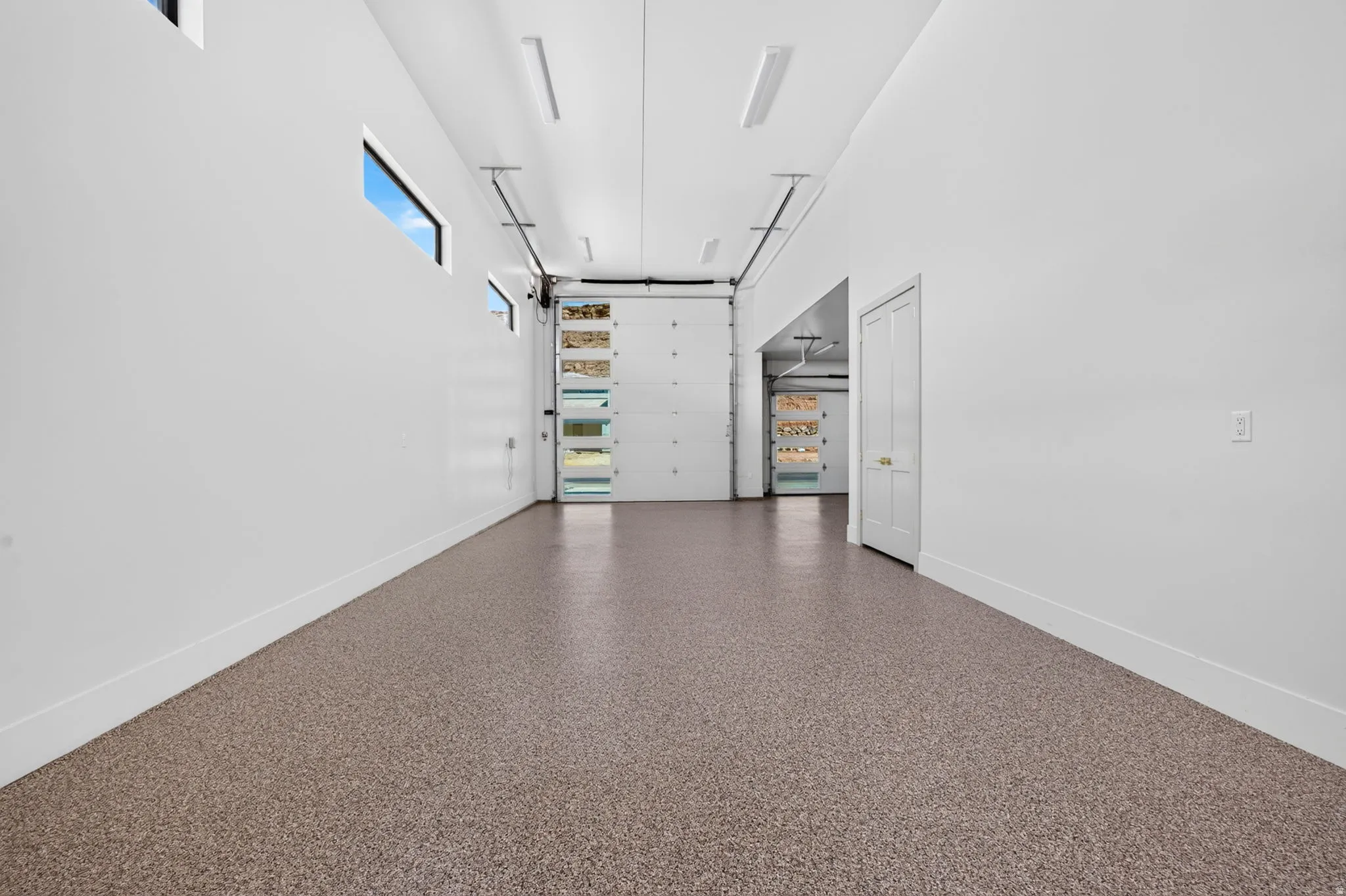 Expansive garage space featuring durable epoxy flooring, multiple linear ceiling lights, and two overhead garage doors with frosted glass panels