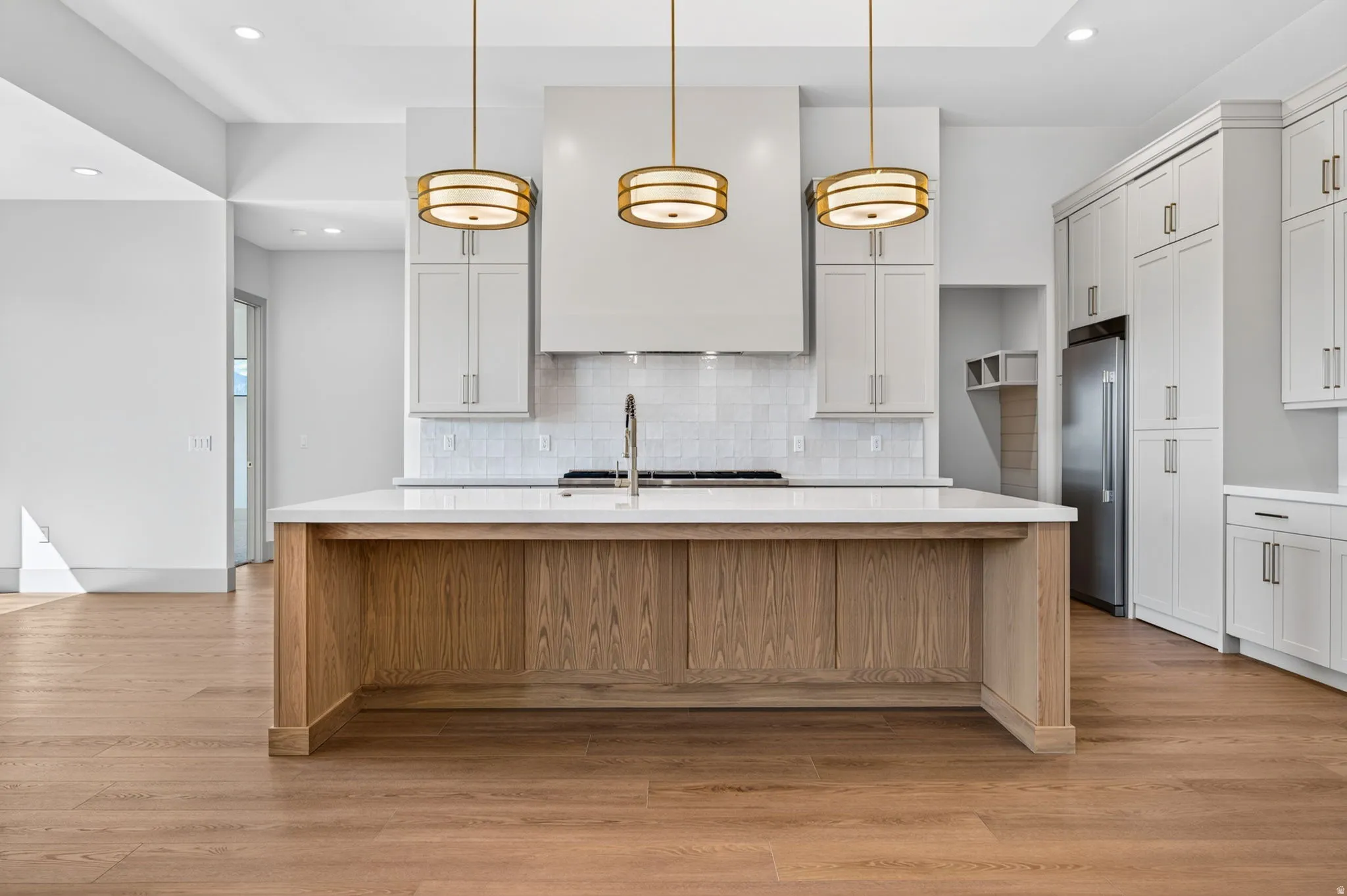 Central kitchen island with a light wood finish and light-toned countertop, complemented by three pendant light fixtures