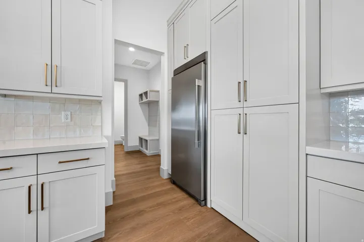 White shaker-style cabinetry, stainless steel refrigerator, light-toned countertop, square tile backsplash, and wood-finish flooring