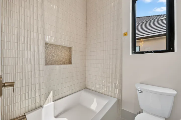 White subway tile surround with integrated shower niche, white bathtub, and contemporary toilet
