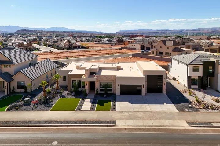 Modern exterior with a stone accent facade, two-car garage, artificial turf lawn, and desert landscaping
