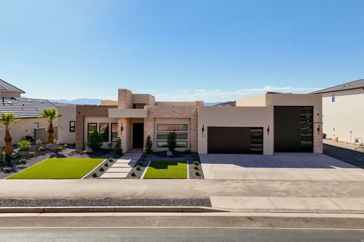 Modern exterior featuring a stucco and stone facade, flat roofline, integrated two-car garage, concrete driveway, and low-maintenance landscaping with artificial turf