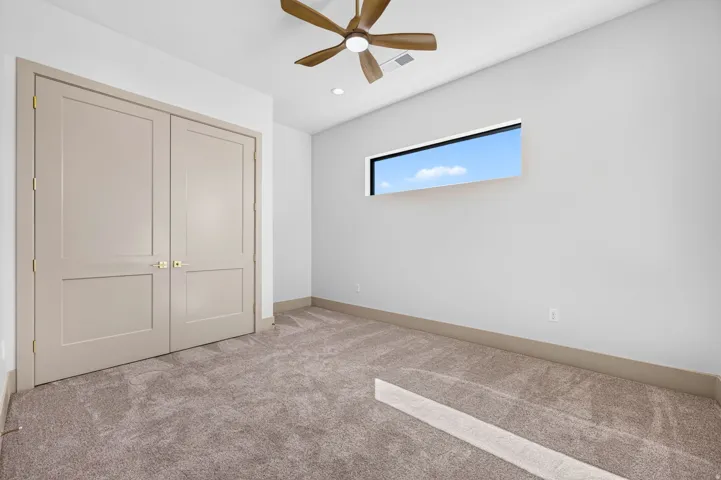 Recessed lighting, wood-finish ceiling fan, horizontal window, neutral carpet, and two-panel double doors with gold-finish hardware