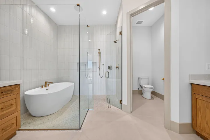Walk-in shower with clear glass enclosure, freestanding soaking tub, and vertical tile accents