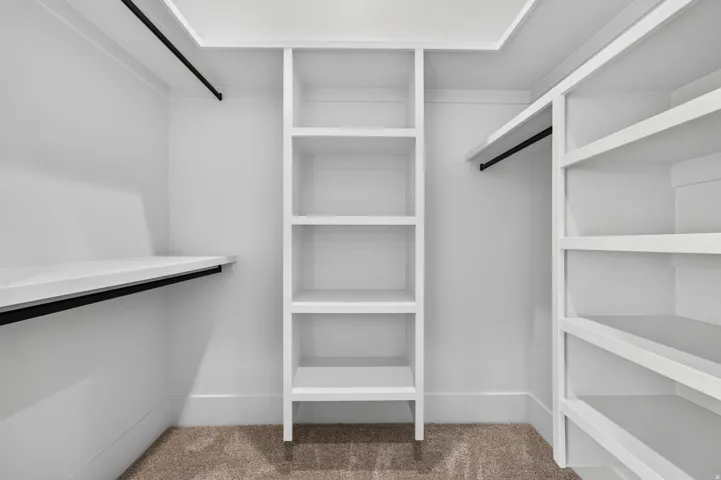 Built-in custom shelving, multiple clothing rods, clean white finish, and neutral carpet