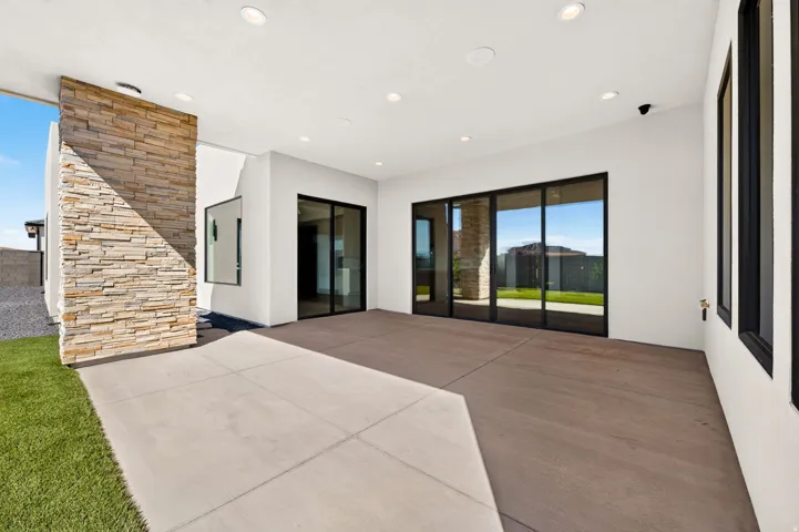 Covered patio with recessed lighting, a stacked stone accent wall, large sliding glass doors, and a concrete slab