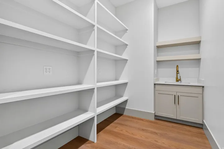 Extensive built-in shelving, wood-finish flooring, integrated sink, gold-finish faucet, and light-colored cabinetry