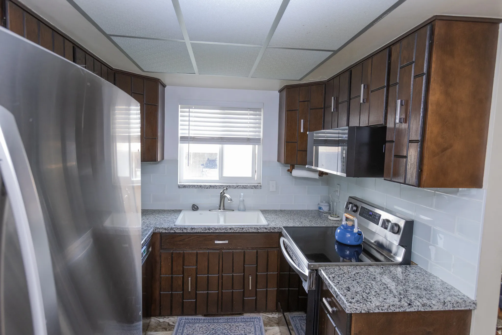 U-shaped kitchen featuring dark wood cabinetry, white subway tile backsplash, granite-finish countertops, and stainless steel appliances