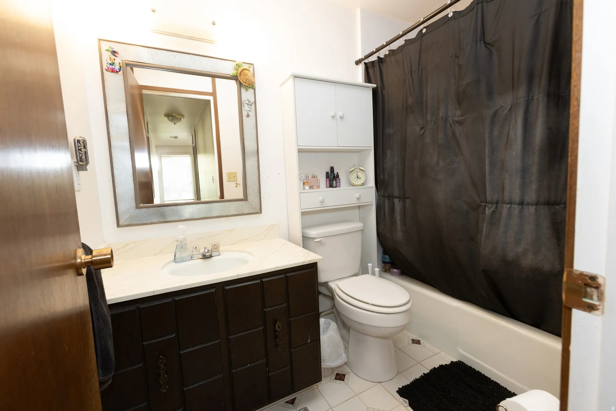 Vanity with integrated sink, framed mirror, built-in shelving, white bathtub, and tile flooring