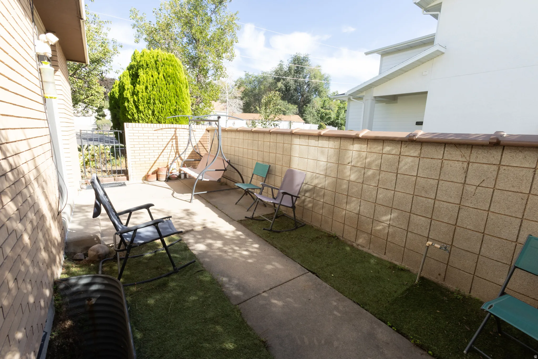 Paved patio area with faux grass accents and a concrete block privacy wall