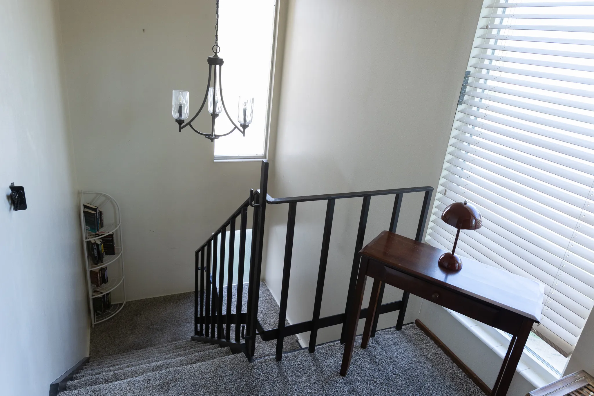 Staircase with carpeted treads, dark metal railing, and a wrought iron chandelier