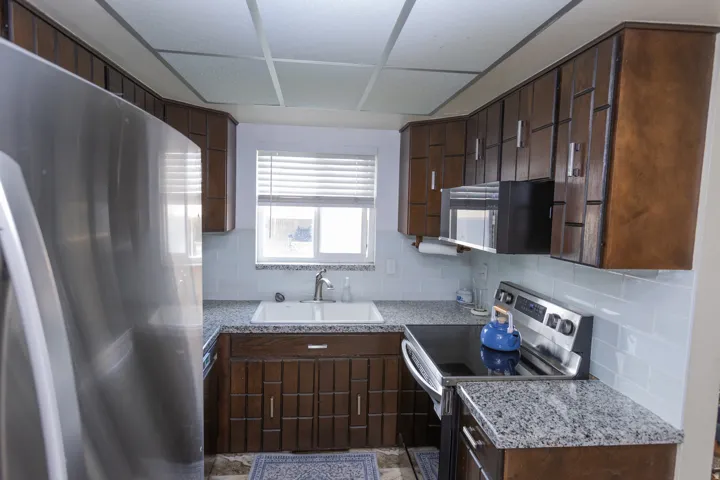 U-shaped kitchen featuring dark wood cabinetry, white subway tile backsplash, granite-finish countertops, and stainless steel appliances