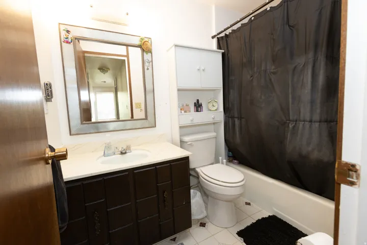 Vanity with integrated sink, framed mirror, built-in shelving, white bathtub, and tile flooring
