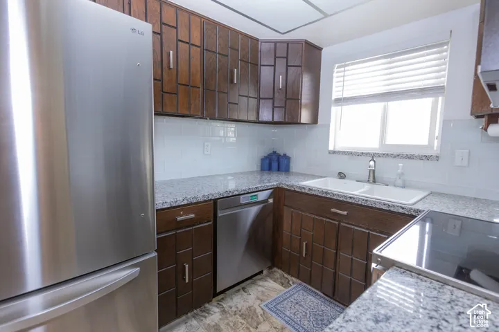 Stainless steel refrigerator, granite-style countertops, subway tile backsplash, dark wood-finish cabinetry, and a dual basin sink