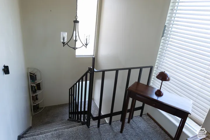 Staircase with carpeted treads, dark metal railing, and a wrought iron chandelier