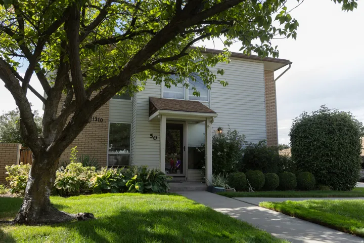 Front entrance featuring a covered porch, established tree, manicured lawn, and mature landscaping