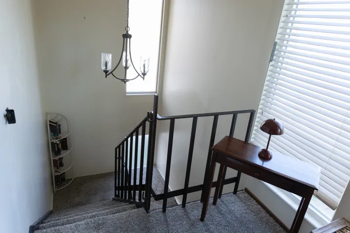 Staircase with carpeted treads, dark metal railing, and a wrought iron chandelier