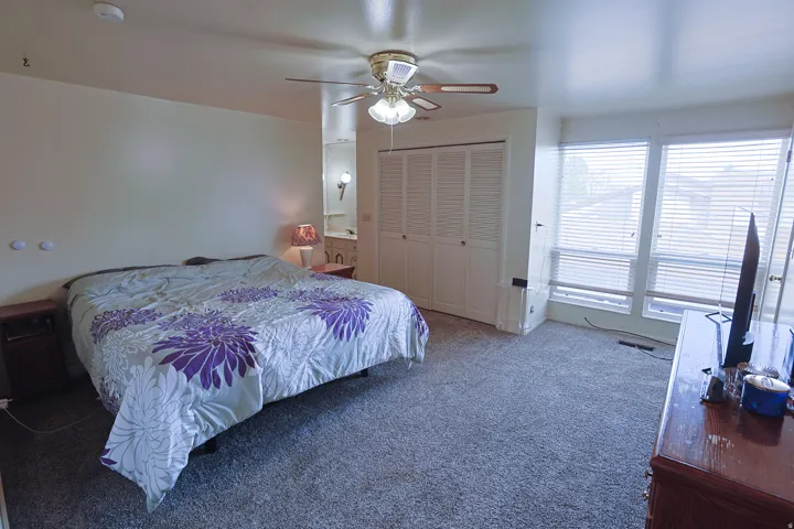 Carpeted flooring, ceiling fan with integrated lighting, multiple windows with blinds, and bi-fold closet doors