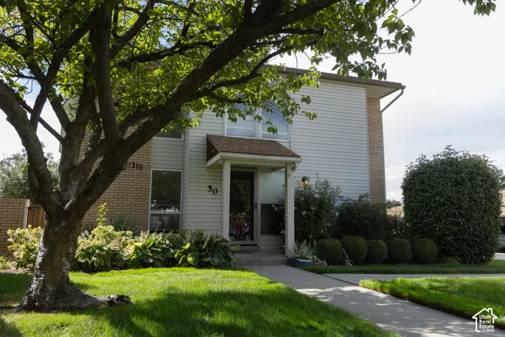 Front entrance featuring a covered porch, established tree, manicured lawn, and mature landscaping
