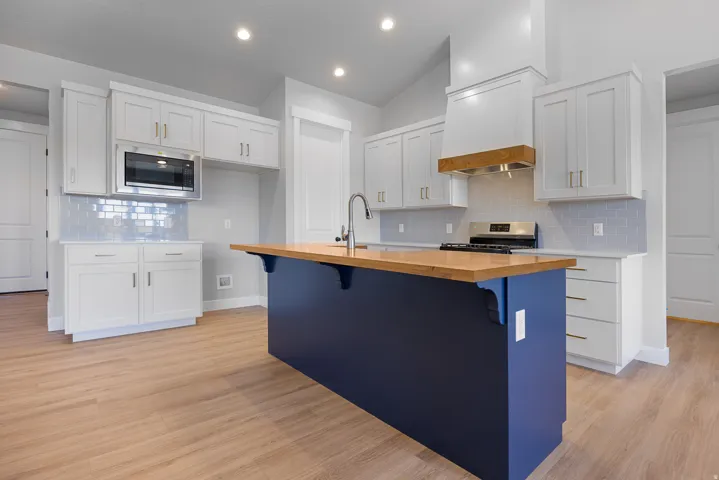 Kitchen featuring white shaker cabinetry, stainless steel appliances, light wood-finish flooring, a wood-finish island countertop, and a blue island base