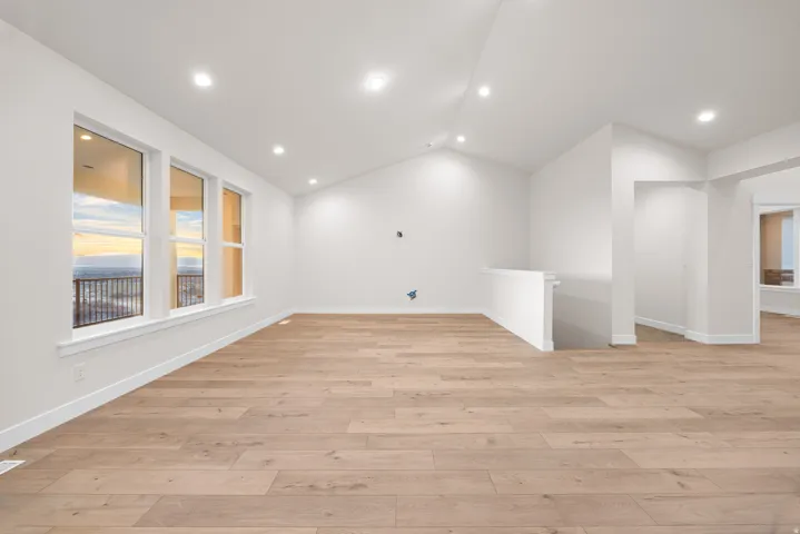 Vaulted ceilings with recessed lighting, wood-finish flooring, white walls, and multiple windows