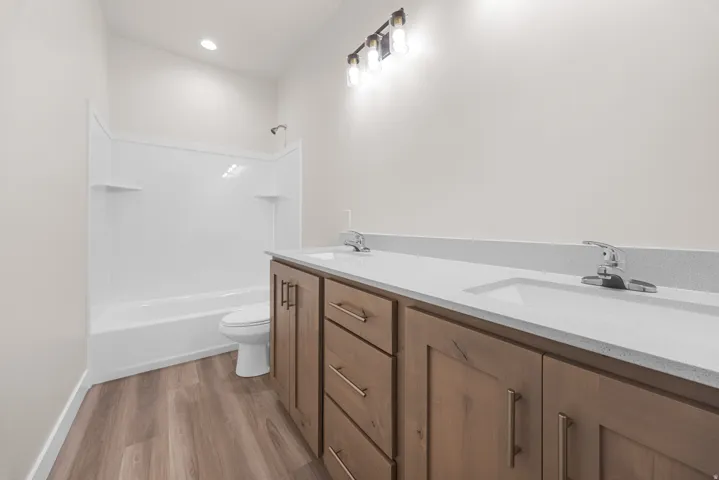 Dual-sink vanity with wood-finish cabinetry, light-colored countertops, and chrome fixtures