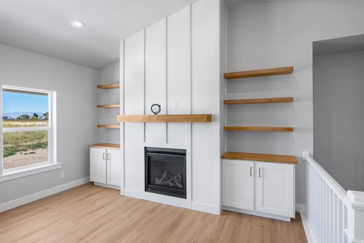 Fireplace with wood-finish mantel, built-in cabinetry, wood-finish flooring, recessed lighting, and a visible window