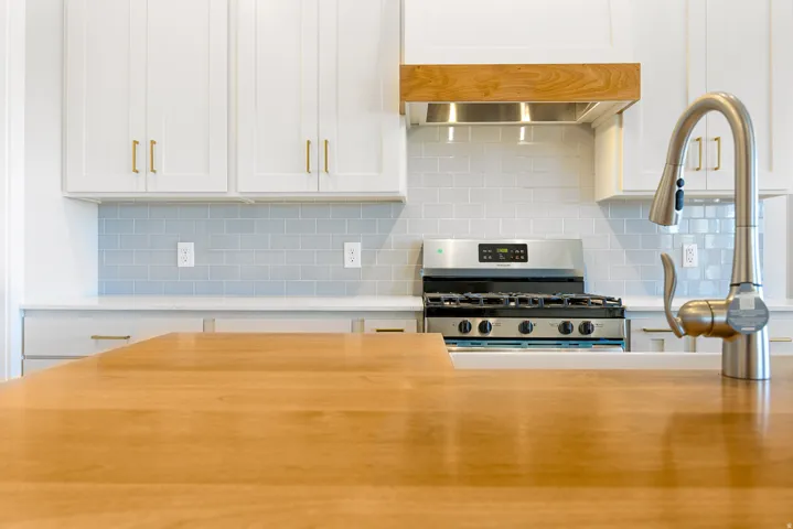 White cabinetry with gold-finish hardware, light wood-finish countertops, stainless steel range, and a brushed nickel pull-down faucet