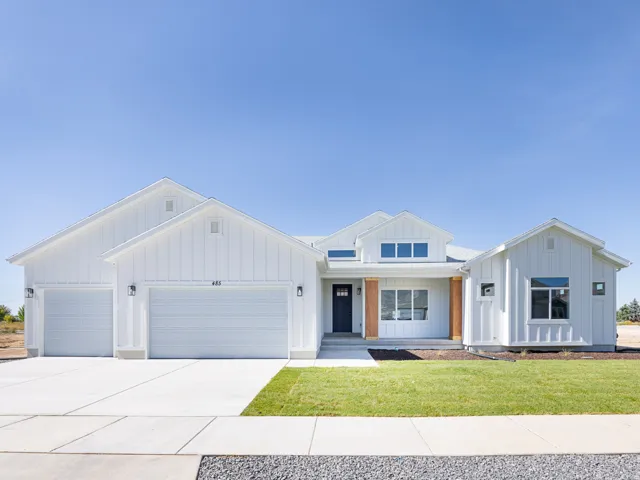 Modern farmhouse exterior featuring white board and batten siding, a three-car garage, multiple gables, and a prominent front entrance with natural wood accents