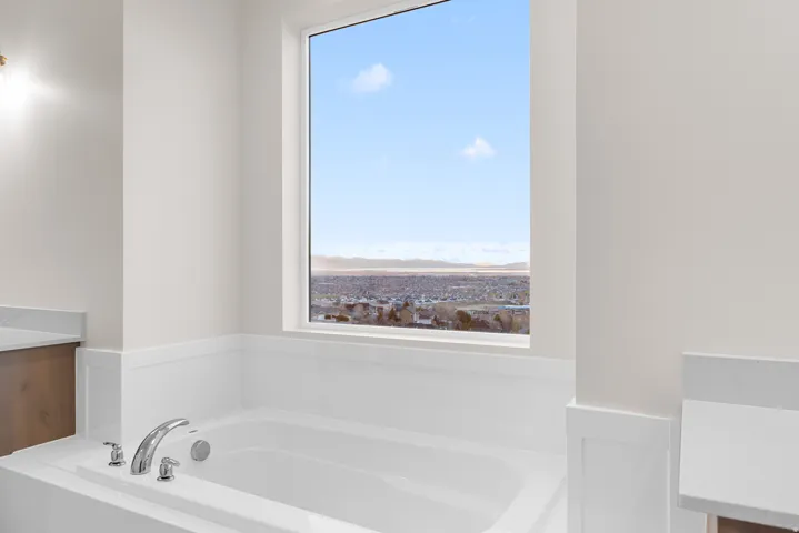 Built-in soaking tub with polished chrome fixtures, surrounded by white wainscoting and light-toned walls
