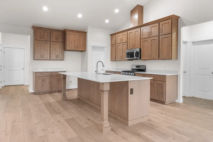 Spacious kitchen featuring wood-finish flooring, light wood cabinetry, white countertops, and a kitchen island with a built-in sink