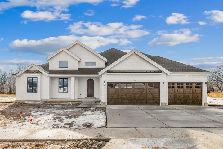 White brick exterior with a dark shingle roof, arched wood-finish front entry door, and wood-finish garage doors
