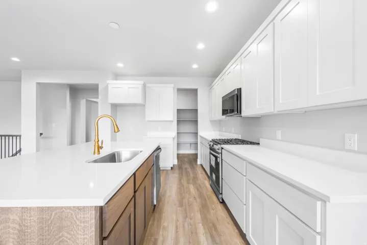 Kitchen featuring white shaker cabinetry, white countertops, stainless steel appliances, a gold-tone gooseneck faucet, and wood-finish flooring
