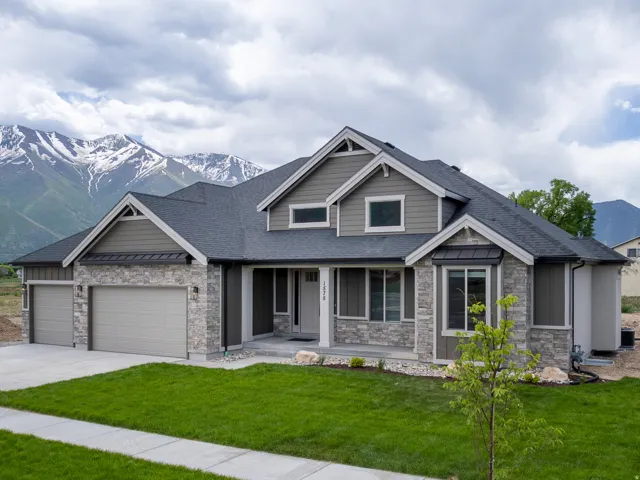 New construction residence featuring a stone and siding exterior, an attached multi-car garage, and a manicured lawn