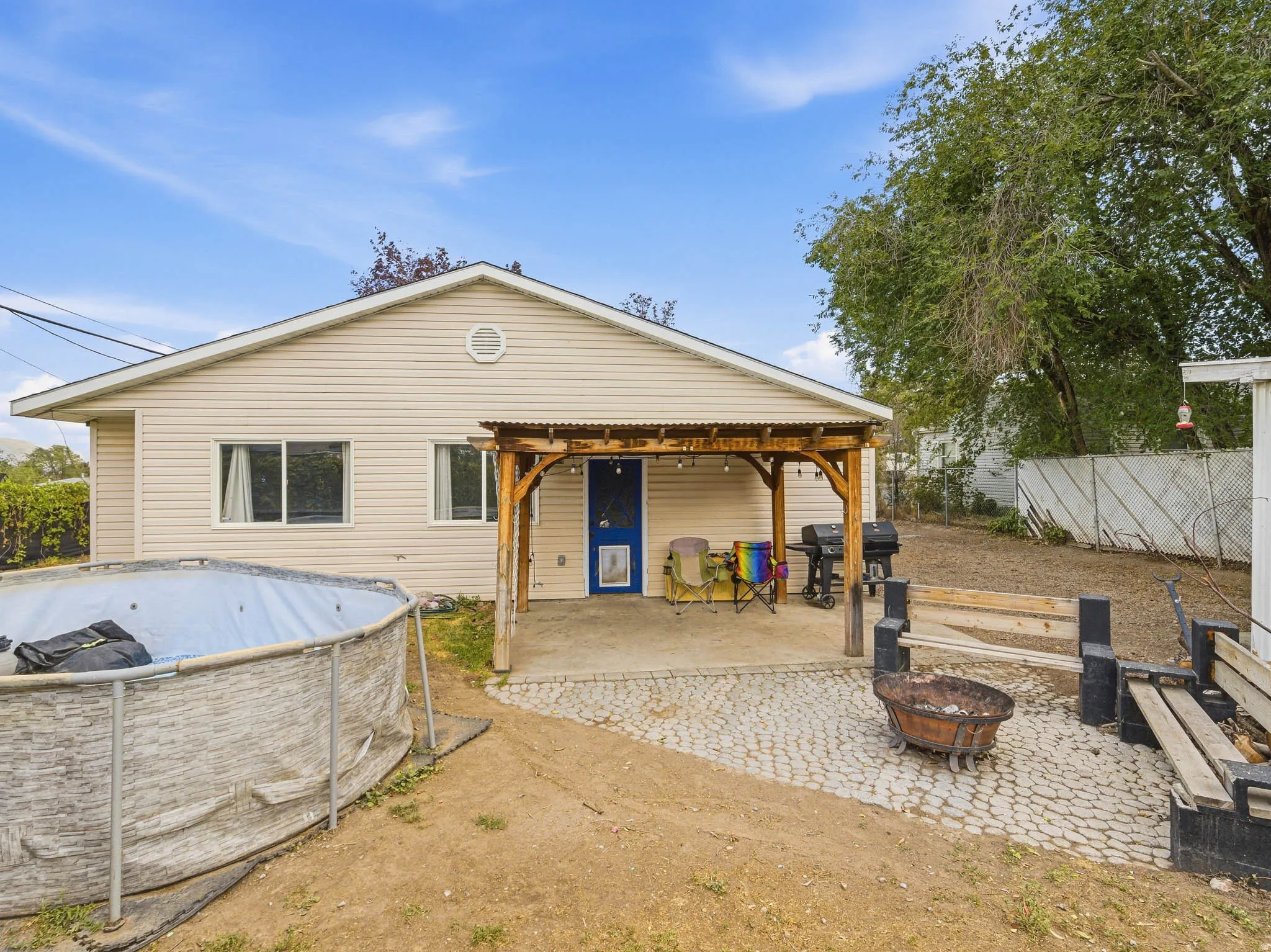 Rear exterior with horizontal siding, a covered patio with wood supports and a corrugated roof, and a paved patio area