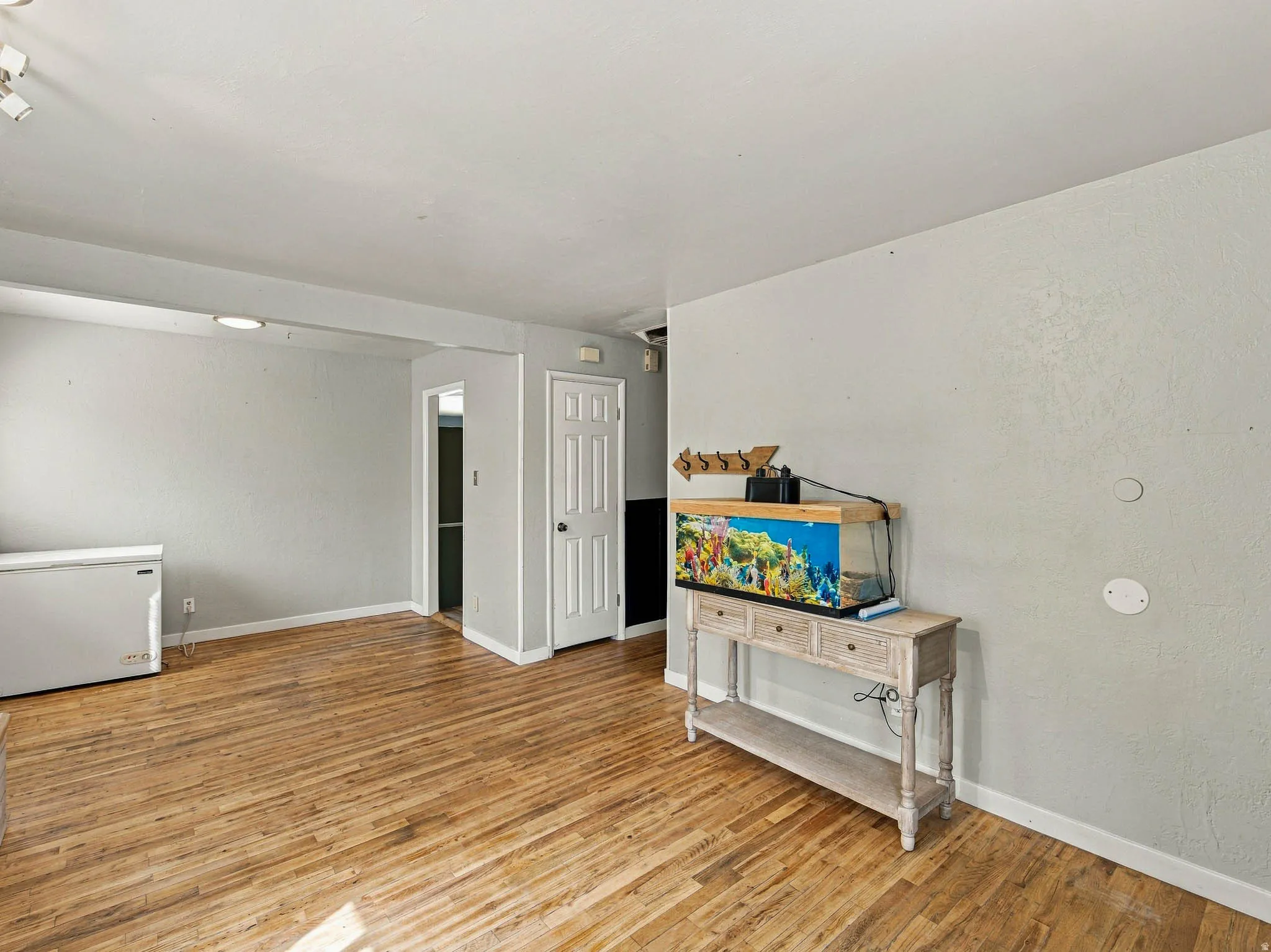 Wood-finish flooring with white trim, track lighting, and a paneled interior door