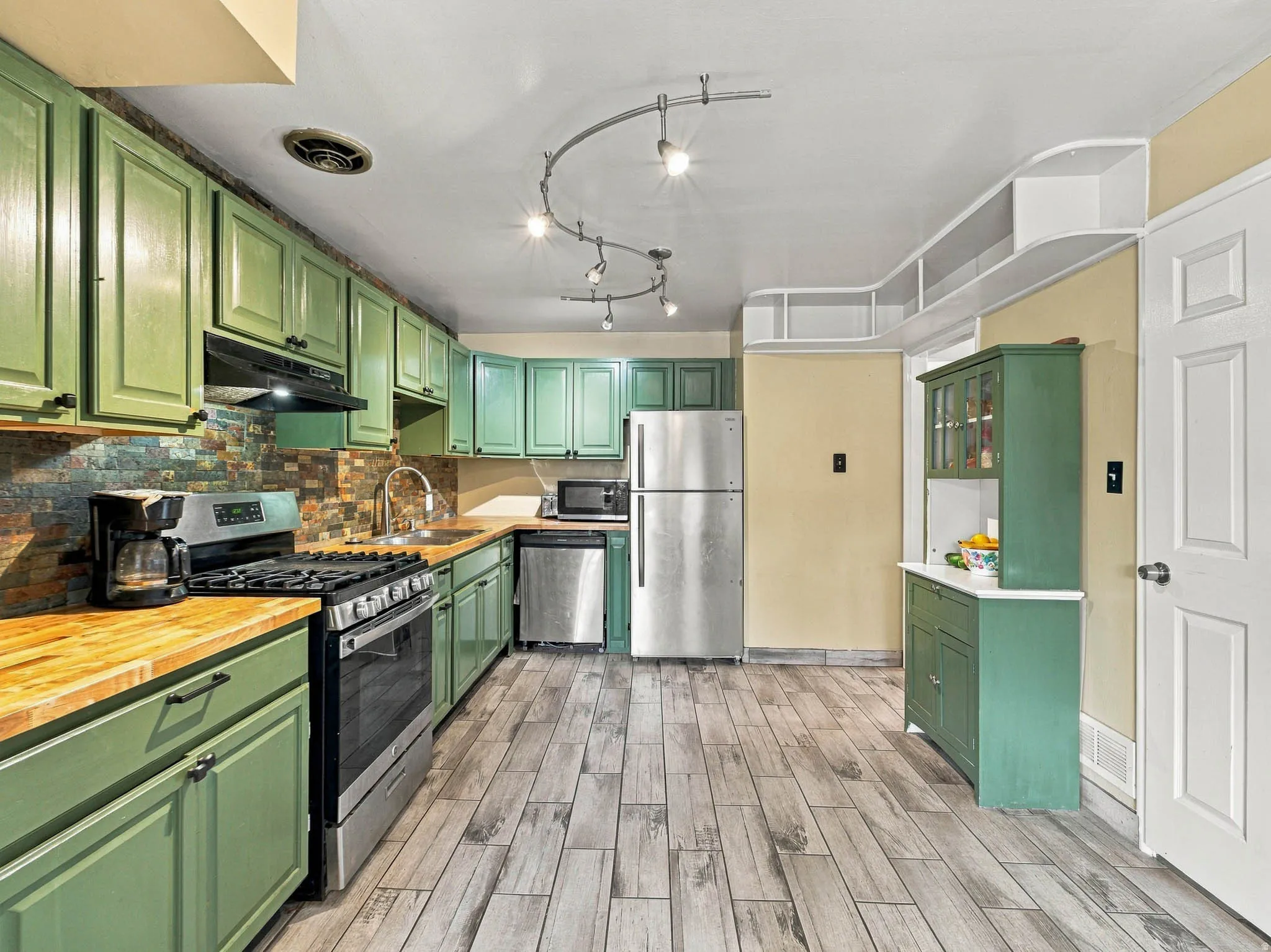 Kitchen featuring a gas range, stainless steel appliances, wood-finish flooring, and track lighting