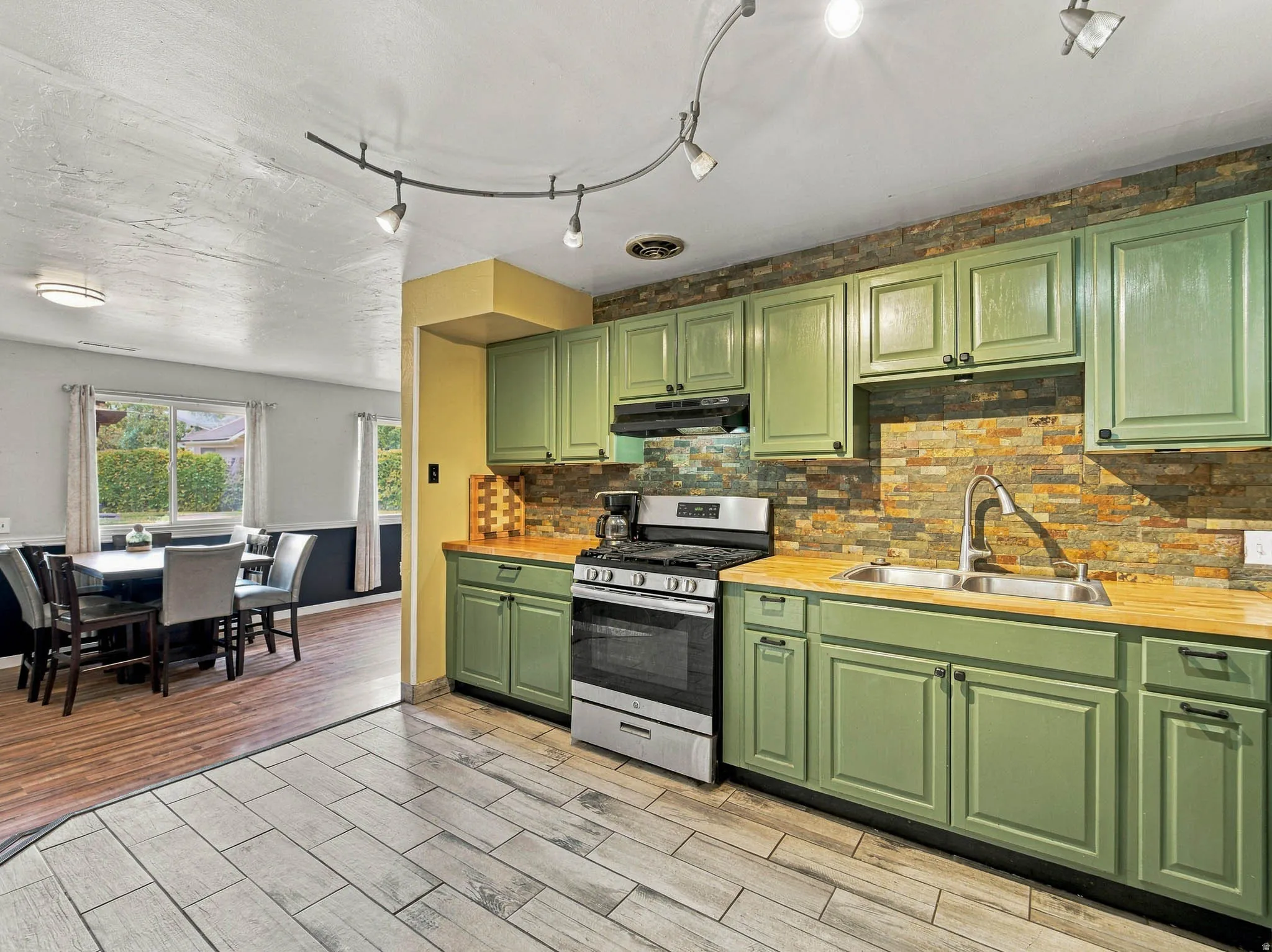 Kitchen featuring green cabinetry, wood-finish countertops, a stainless steel range, and a stacked stone backsplash