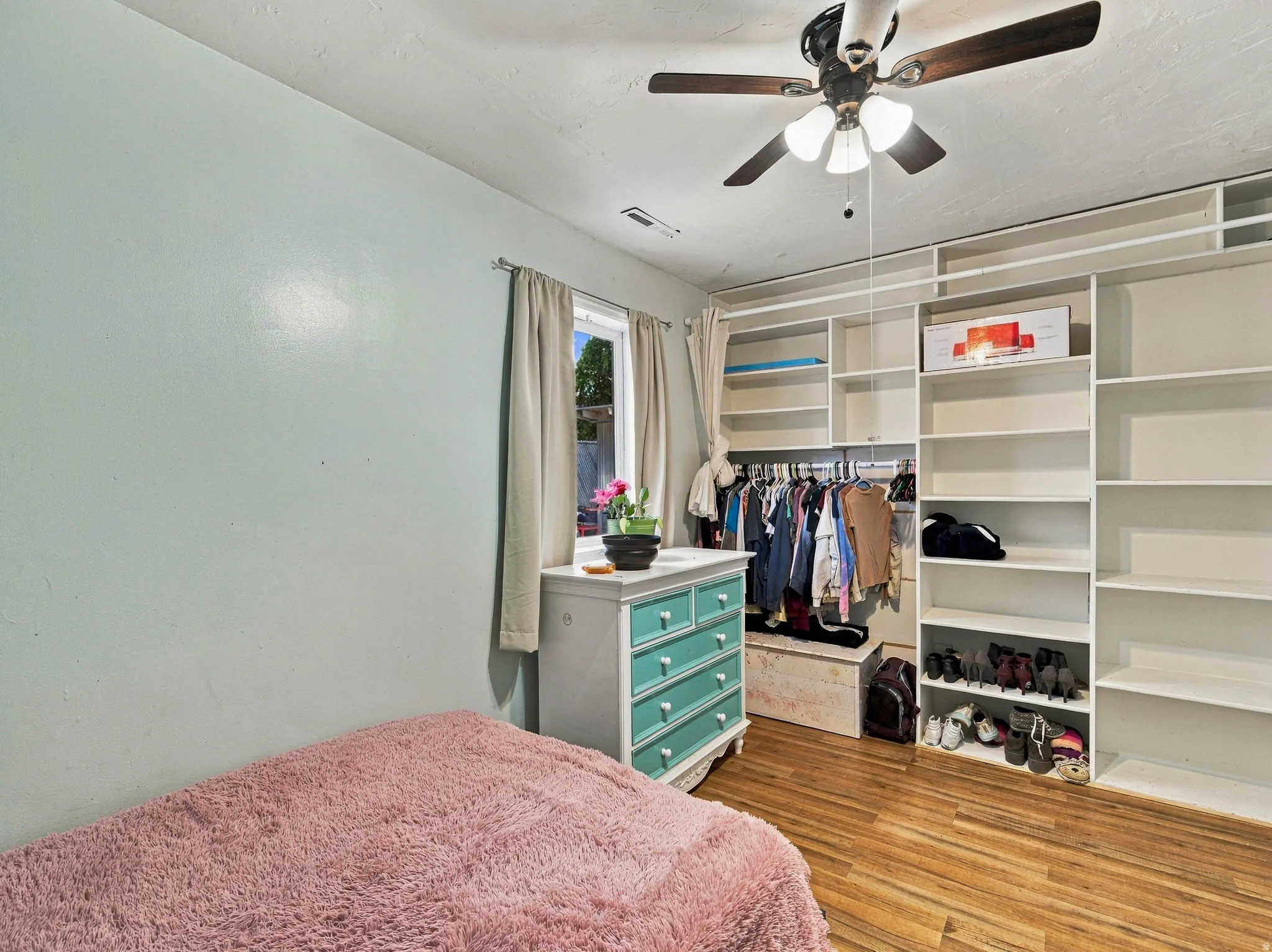 Wood-finish flooring, built-in shelving, built-in clothing racks, ceiling fan with light fixture, and window with natural light