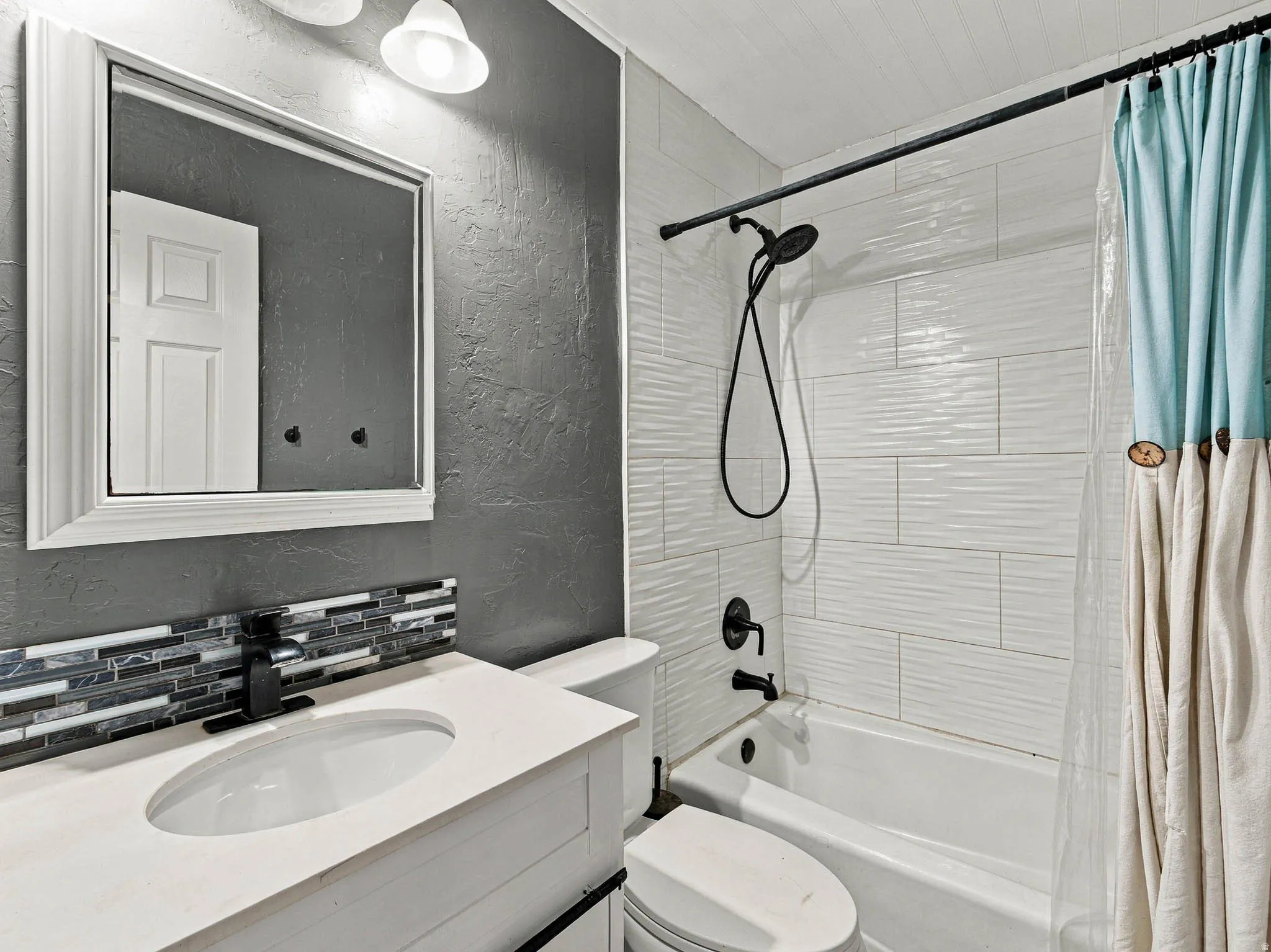 White vanity with an integrated sink, mosaic tile backsplash, and matte black faucet