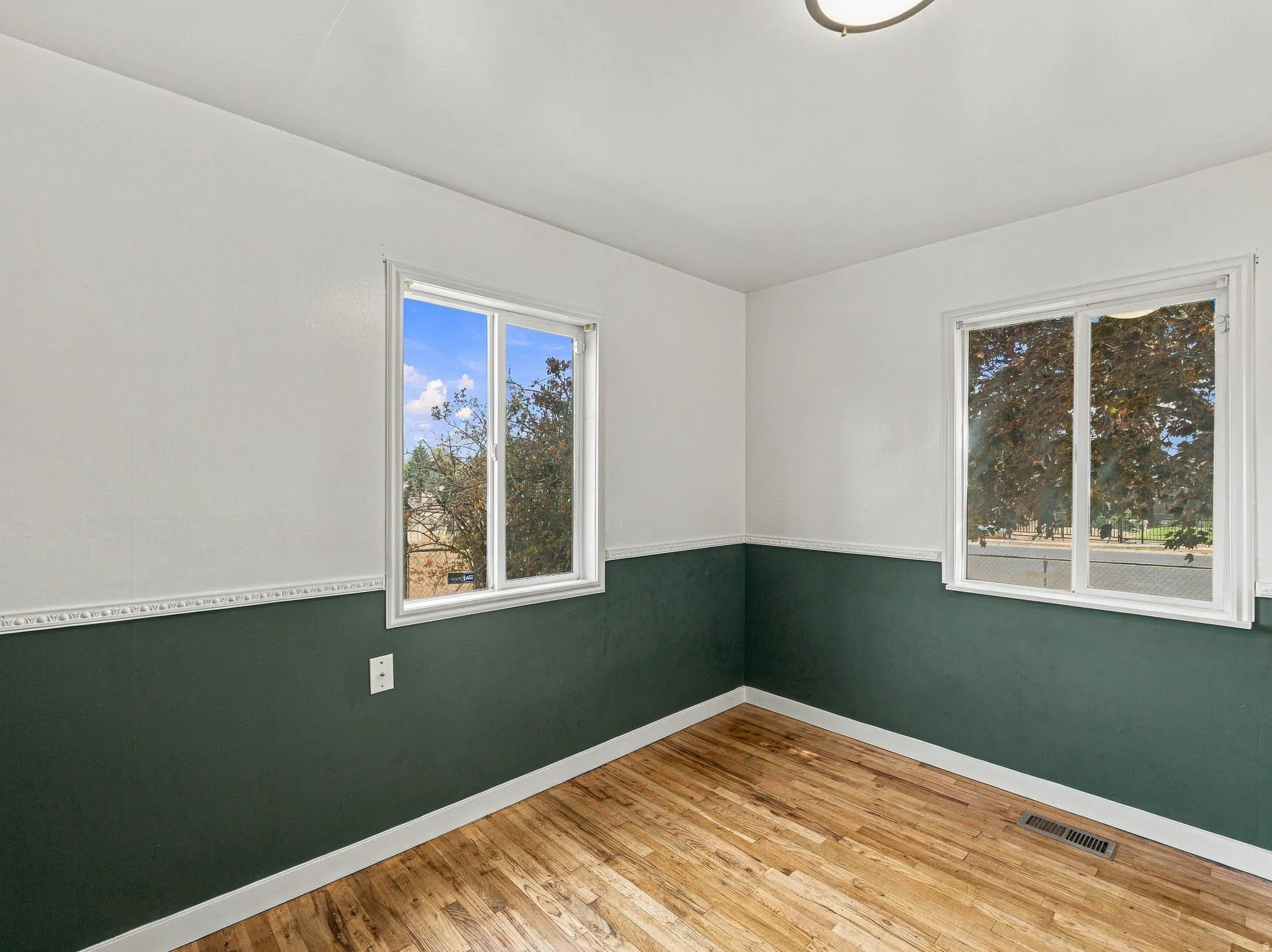 Wood-finish flooring, two large windows, white trim, two-tone wall paint, and a ceiling-mounted light fixture