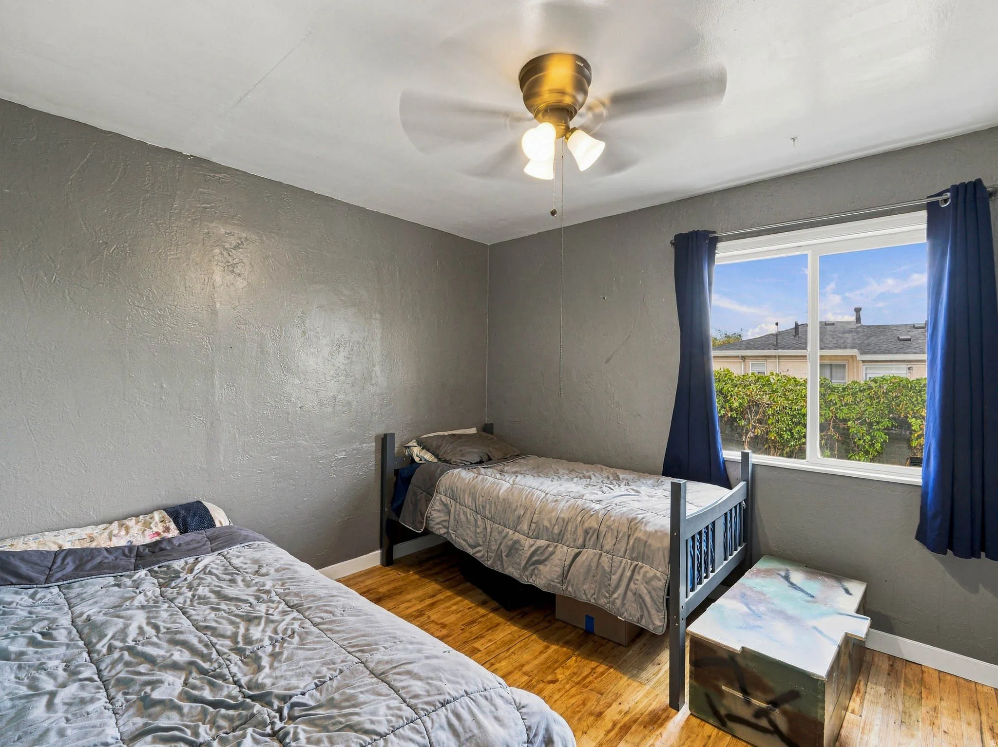 Wood-finish flooring with a textured wall finish, featuring a ceiling fan with light fixture and a window with white trim