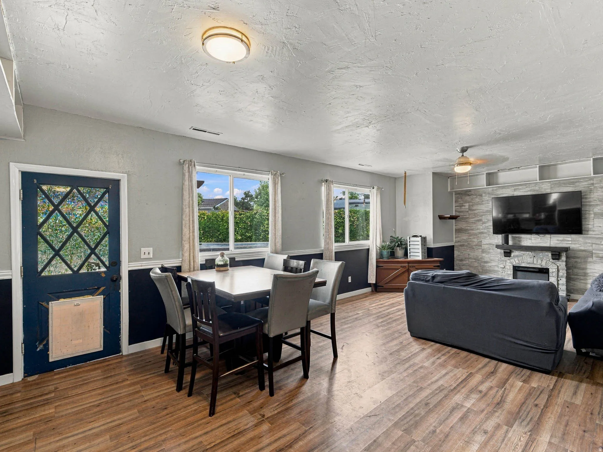 Open-concept living area featuring wood-finish flooring, a stone-clad fireplace, and a ceiling fan