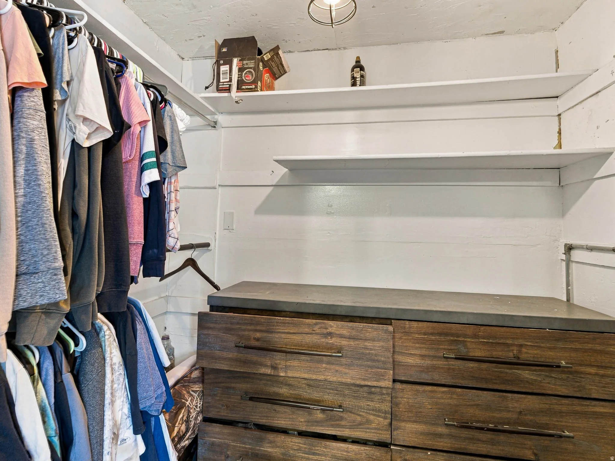 Built-in wood-finish dresser with dark hardware, white wall shelving, and overhead lighting