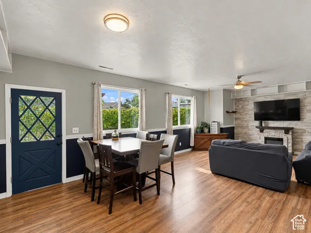 Open-concept interior featuring wood-finish flooring, a textured stone fireplace surround with a wood mantel, dual-tone wall paint with chair rail molding, ceiling-mounted lighting, and a solid exterior door with diamond-patterned glazing