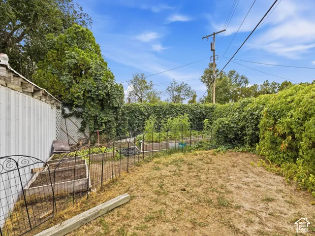 Enclosed backyard featuring mature perimeter foliage, raised garden beds, and decorative metal fencing