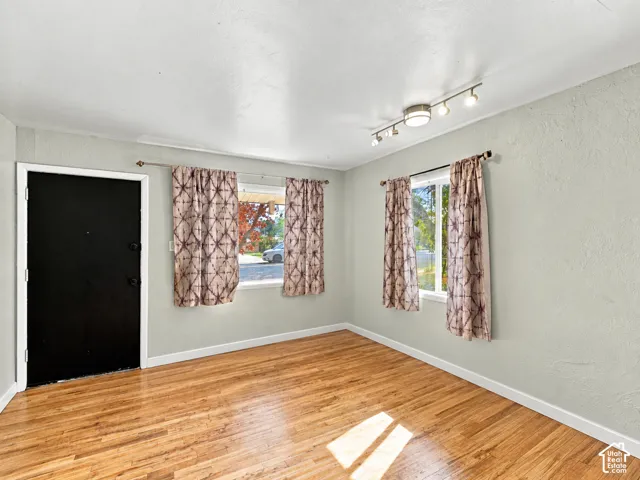 Living area featuring wood-finish flooring, textured walls, two windows with metal curtain rods, and a multi-directional track lighting fixture