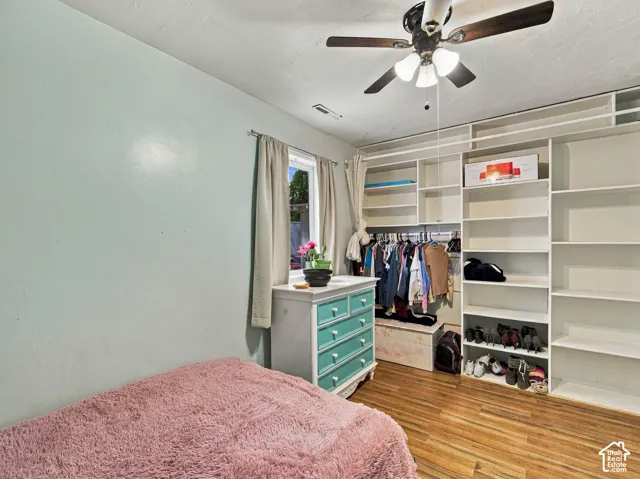 Wood-finish flooring, built-in shelving, built-in clothing racks, ceiling fan with light fixture, and window with natural light