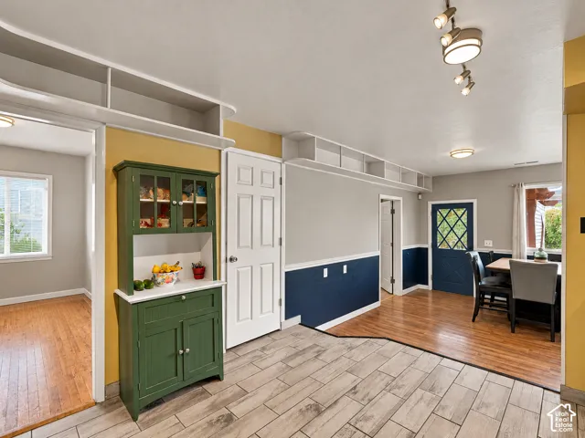 Built-in green cabinetry with glass-front display, overhead storage shelving, wood-finish flooring, ceramic tile flooring, and multi-light track lighting