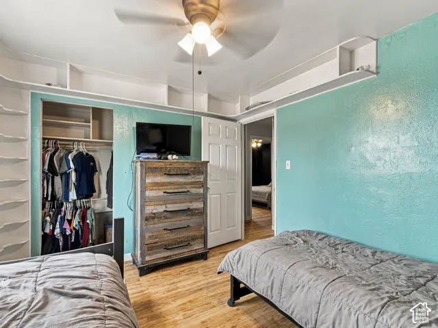 Built-in shelving, wood-finish flooring, ceiling fan, and built-in closet with shelving